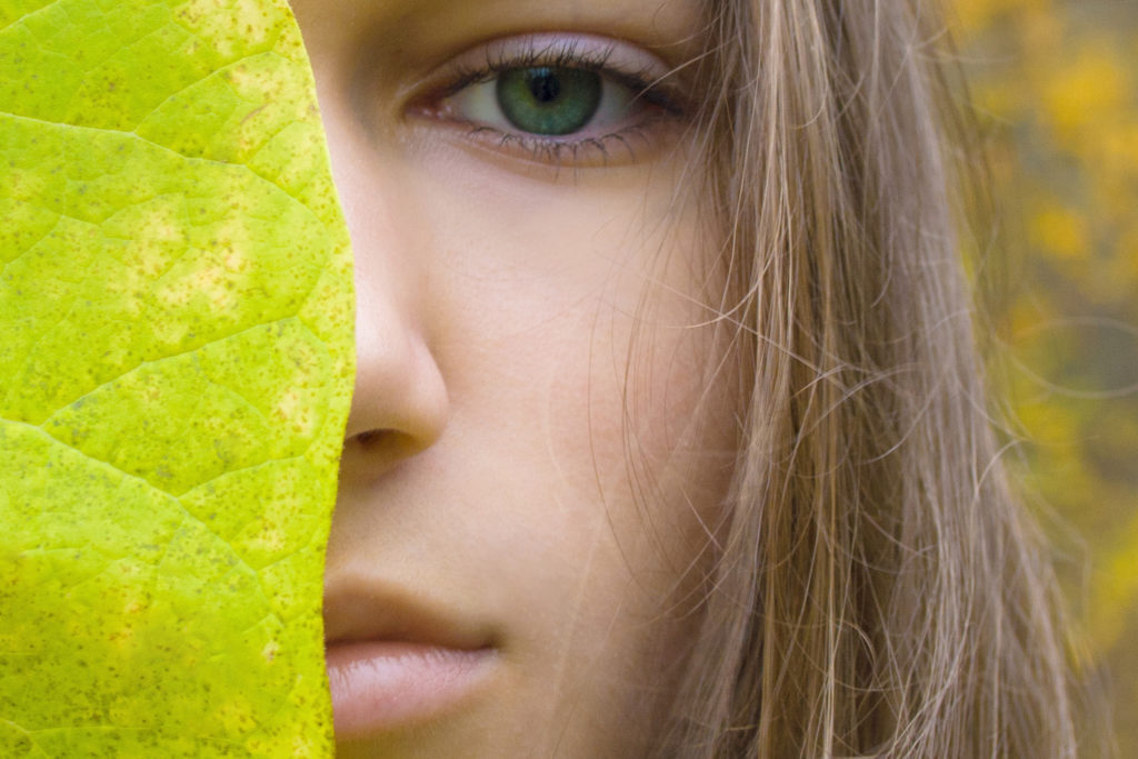 Beauty young blonde women with green eyes. Teen girl model and green leaf on autumn yellow forest background. Concept of Spa, skin care, wellness, nature organic cosmetic and environmental protection.